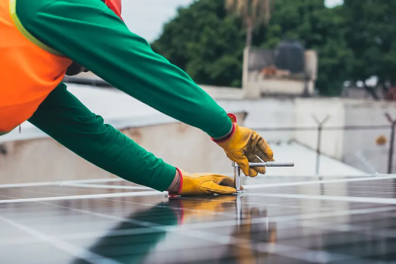 Technician in gloves securing a solar panel to its rail