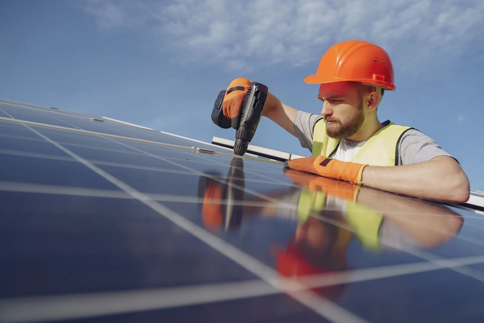Solar technician in a hard hat working on a panel under a blue sky