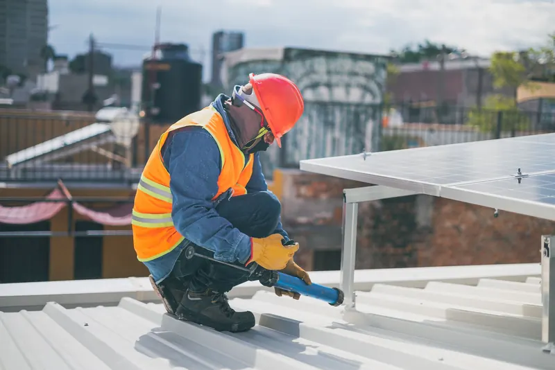 Technician kneeling on a roof beside solar racking